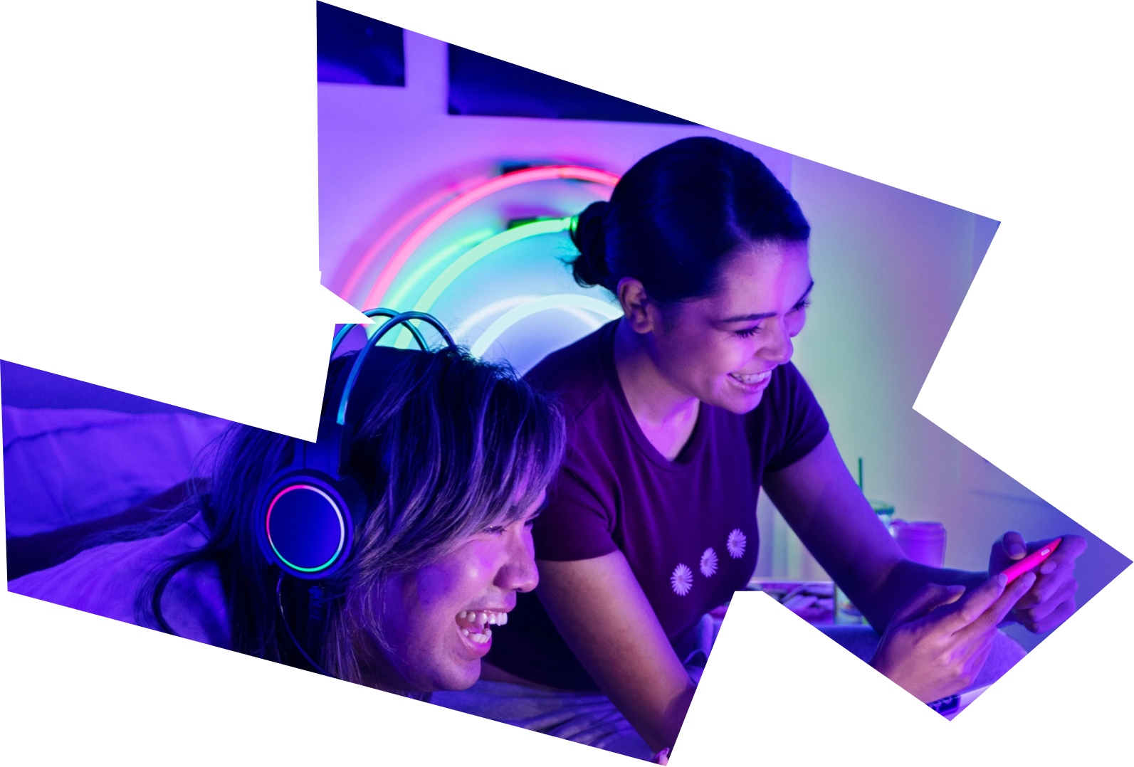 Two young women smile and laugh together as they view and listen to ByteDance content on a smartphone and computer.